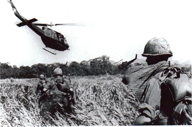 A helicopter flying over a field with soldiers.